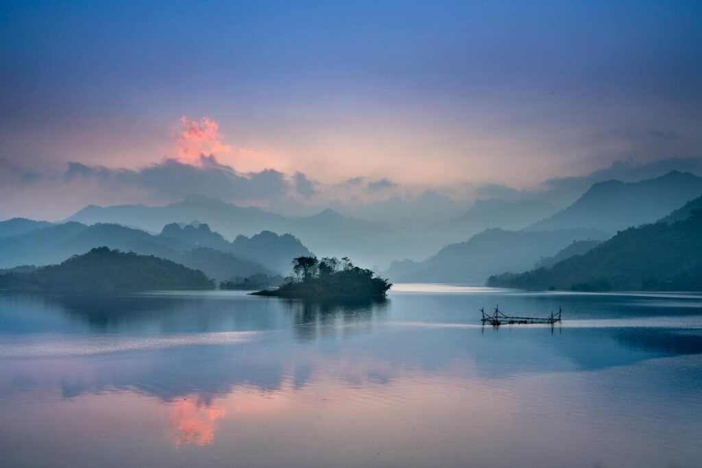 Tranquil lake with misty mountains at sunrise in Thượng Lâm, Vietnam.