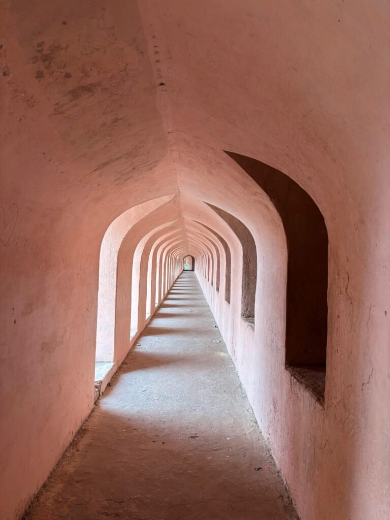 A timeless arched corridor showcasing classic Indian architecture with pink walls and columns.