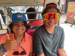 Caleb and Micah smiling and giving a thumbs up while riding in an auto rickshaw on a busy street in India