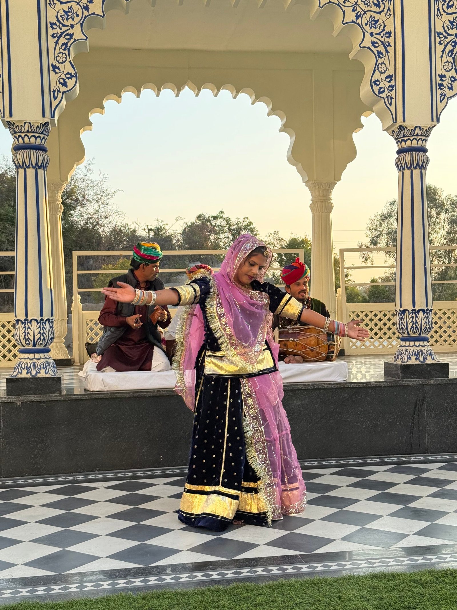 A dancer in a pink and gold costume performing under a white arch