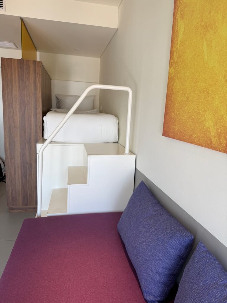 Twin bed tucked into a nook above the couch, with steps and a handrail