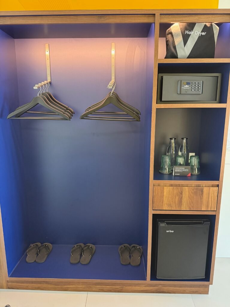 Open closet with hangers, slippers, a safe, water and a fridge