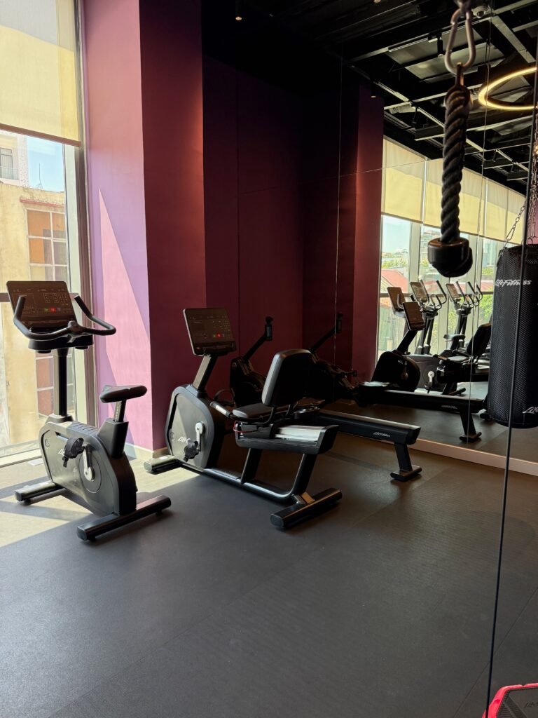 Hotel gym with bikes, a rower and treadmills by the windows